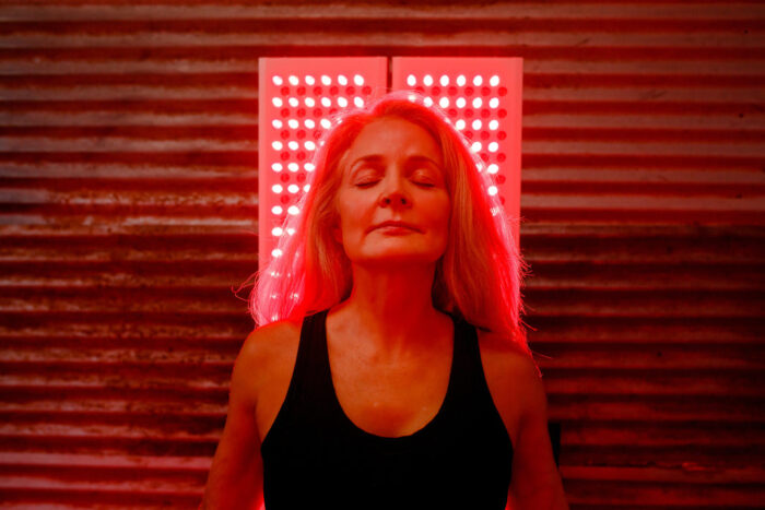 Older woman in sauna with eyes closed standing in front of a MitoPro red light therapy panel