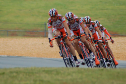 Racing bicyclists in a row on a road all tilted at the same angle to their right sides