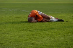 Soccer player lying on green field, holding his head in his hands