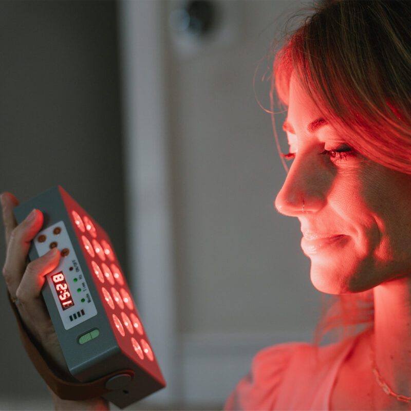 Woman using small red light therapy on face