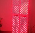 Large red light therapy panel with hundreds of lights on portable stand in darkened room